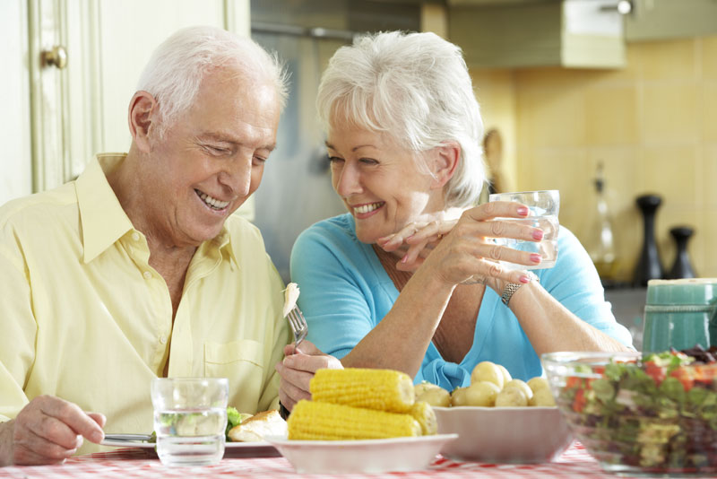 an older couple smiling at each other while they are dining because their implant supported dentures have improved their smiles.